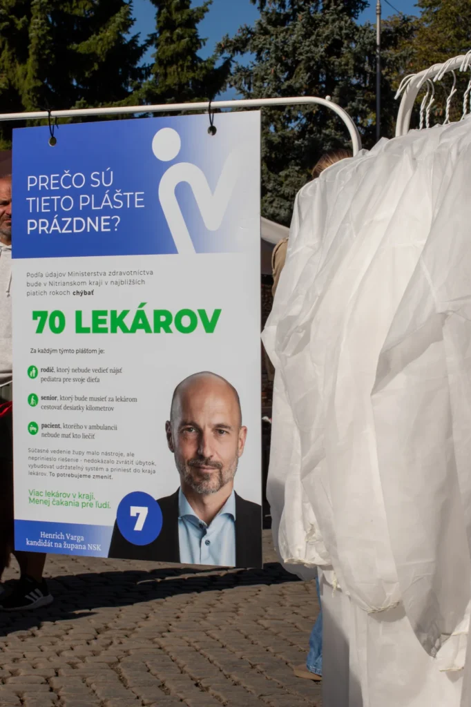 Medzi ľuďmi Panel „Prečo sú tieto plášte prázdne?“ a vešiaky s prázdnymi lekárskymi plášťami na Oberačkových slávnostiach v Nových Zámkoch, 26. 9. 2026